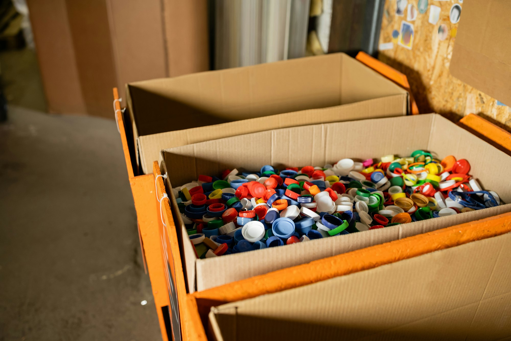 Cardboard boxes with colorful plastic caps for recycle in blurred waste disposal station
